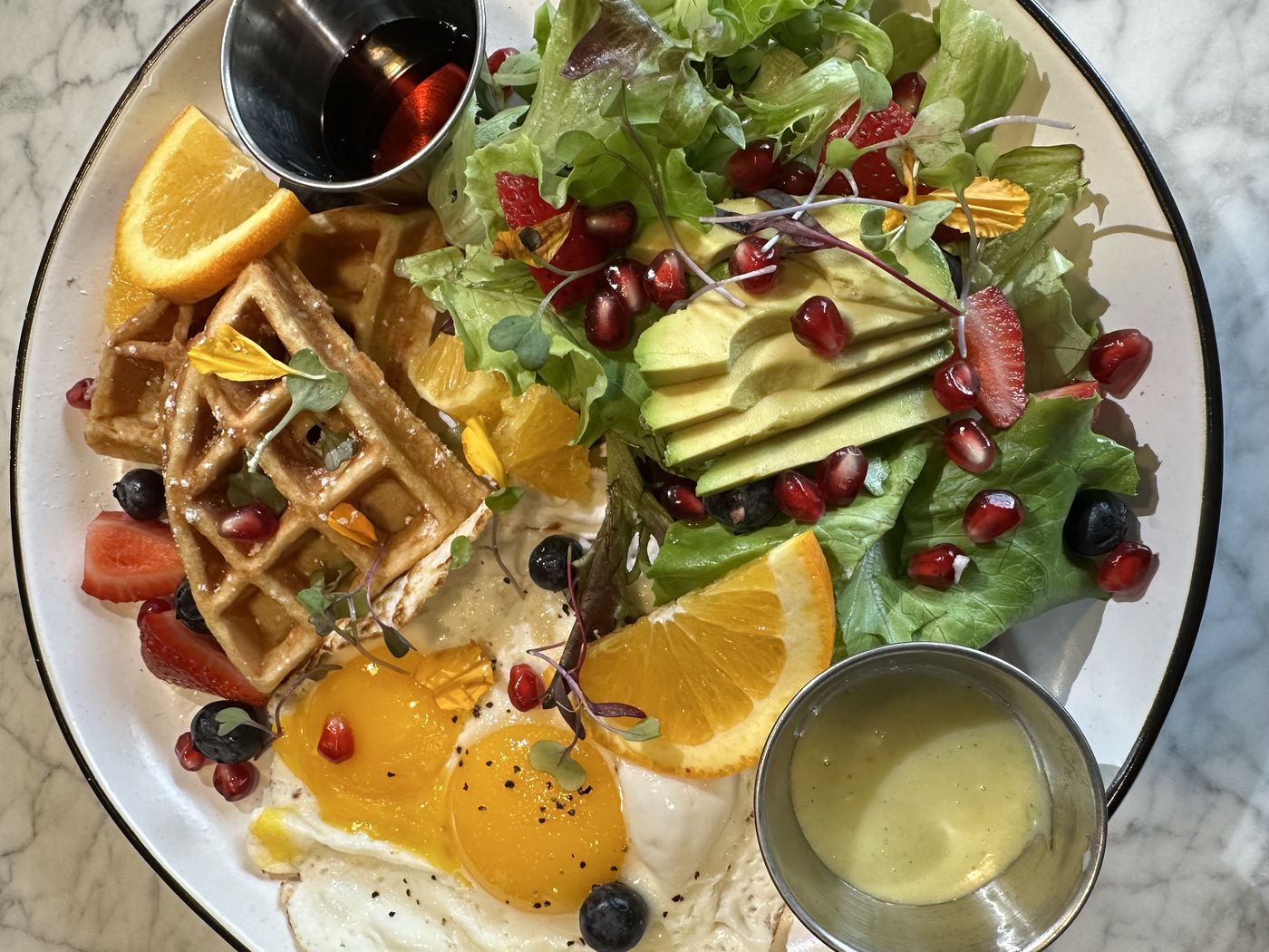 Breakfast plate with waffle, fried eggs, avocado salad, and fruit